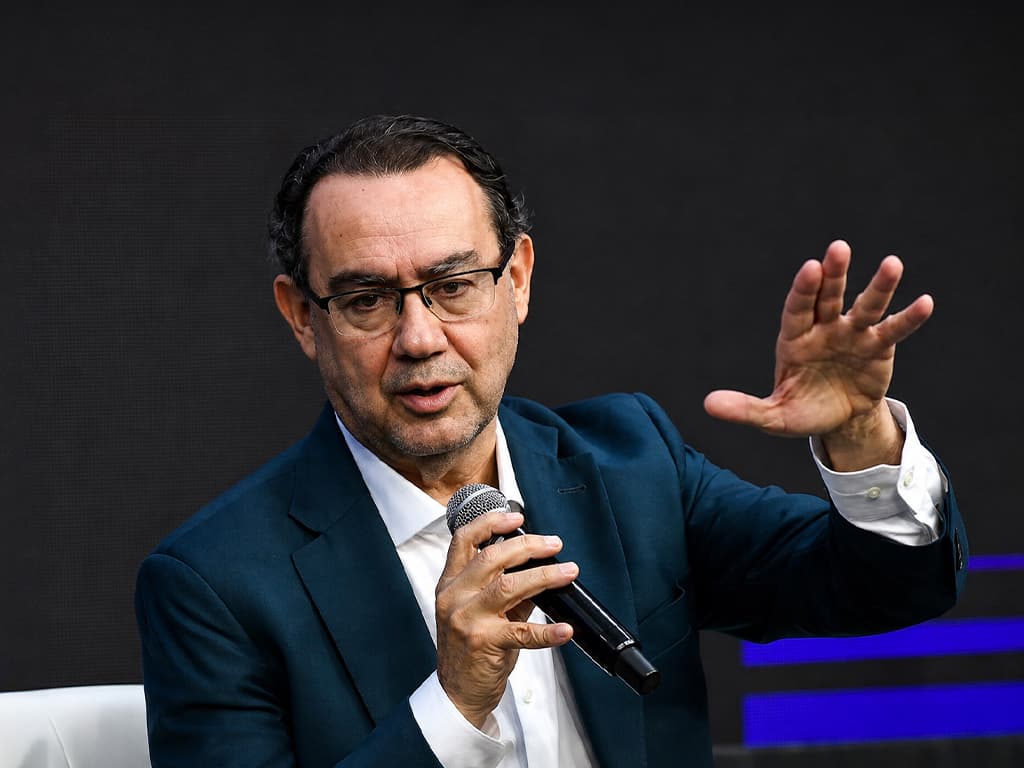 Augusto Cury, de terno azul e óculos, gesticula enquanto fala ao microfone durante um evento.